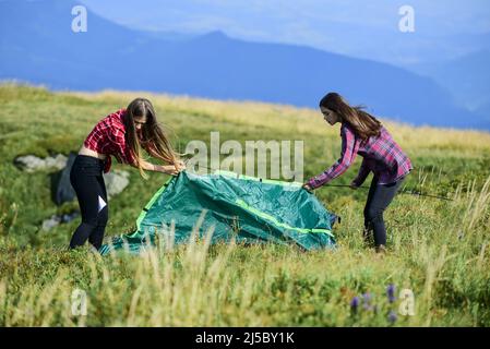 Helpful to have partner for raising tent. Camping skills concept. In middle of nowhere. Girls set up tent on top of mountain. Camping and hiking Stock Photo