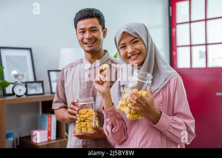 muslim couple holding idul fitri snack smiling to camera Stock Photo