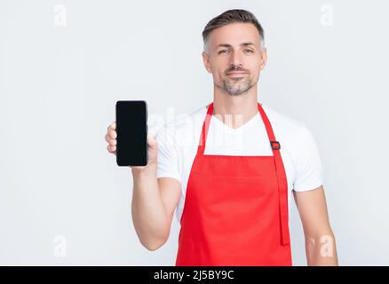 smiling mature man in apron presenting smartphone with copy space Stock Photo