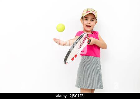 Studio shot of a little smiling girl dressed in pink T-shirt and white skirt - sportswear for tennis on a white background. She stands with a tennis Stock Photo