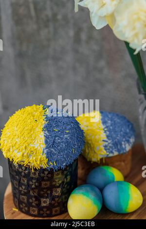 Delicious Easter cakes in the colors of the flag of Ukraine, yellow-blue colored Easter eggs on a wooden table with flowers in the background. place f Stock Photo