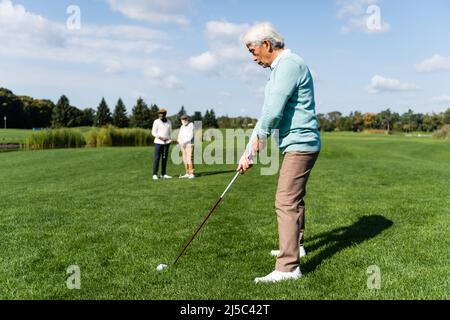 senior asian man playing golf near friends on blurred background Stock Photo