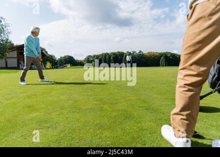 senior asian man playing golf with wealthy interracial friends on lawn Stock Photo