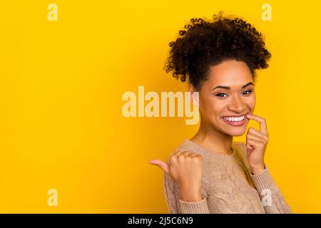 Photo of pretty tricky lady dressed beige pullover pointing empty space finger lips isolated yellow color background Stock Photo