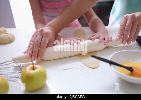 Mom and daughter roll out the dough with rolling pin in kitchen Stock Photo