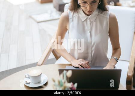 young woman using a laptop at a cafe while drinking a cup of tea. Stock Photo