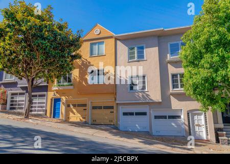 Townhouses on a sloped land area in San Francisco, California. Row of complex townhouses with attached garage and concrete driveways with trees near t Stock Photo