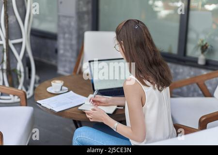 visitor to an Internet cafe making notes in a notebook. Stock Photo