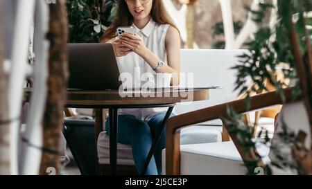 young business woman with a smartphone taking notes in her notebook. Stock Photo