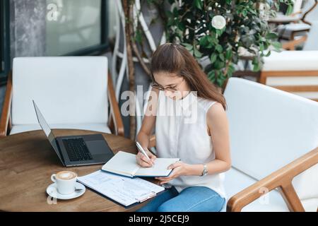 visitor to an Internet cafe is writing something down in her notebook. Stock Photo