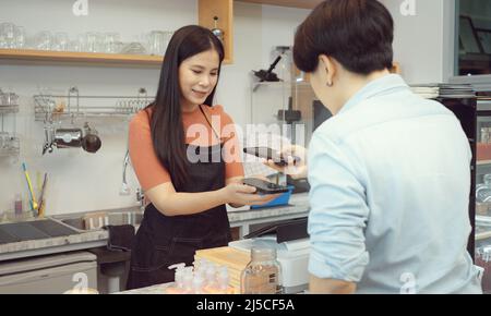 Asian woman customer and barista using smart phone to scan QR code tag on another smart with coffee in coffee shop or restaurant to accepted generate Stock Photo