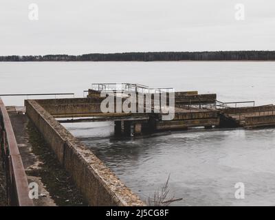 Somber monochromatic landscape with a desolate half-ruined pier in winter. Sense of melancholy and loneliness Stock Photo