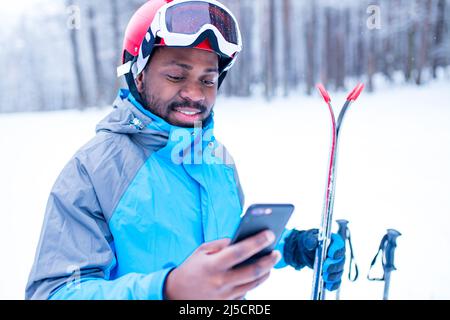 afro american man in blue jacket run ski outdoors in freeze forest holding a phone on hands Stock Photo