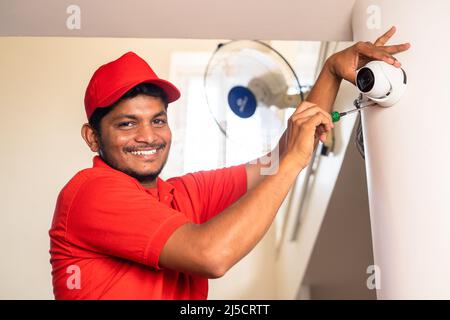 Happy smiling electrician looking at camera while fixing cctv surveillance camera at home - concept of professional occupation, expertise and Stock Photo