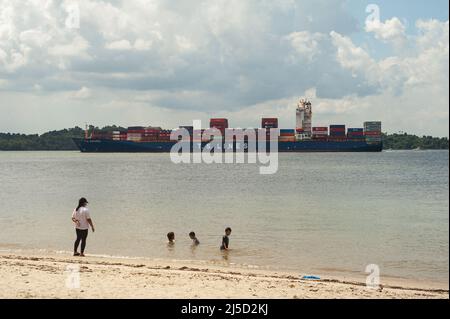 Aug. 10, 2021, Singapore, Republic of Singapore, Asia - People enjoy a day at the beach during the ongoing Corona crisis, swimming in the shallow waters on the shore of Changi Beach Park while a cargo ship passes in the background. Due to the slow spread of the delta variant of the virus, the Southeast Asian city-state still maintains certain restrictions and regulations, such as the wearing of masks outdoors and indoors, and the limited number of people allowed to meet, despite a relatively high vaccination rate of 70% fully vaccinated. [automated translation] Stock Photo