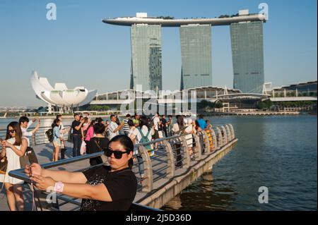18.09.2016, Singapore, Republic of Singapore, Asia - Tourists in Merlion Park on the banks of the Singapore River in Marina Bay with the three skyscraper towers of the Marina Bay Sands Hotel and the ArtScience Museum in the background. [automated translation] Stock Photo
