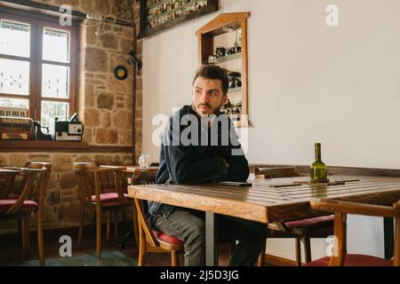 Young man wearing denim clothes waiting for his girlfriend. Worried young man sitting on coffee table looking away. Handsome man sits alone. Divorced Stock Photo