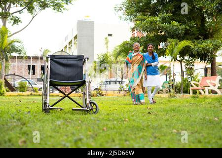 Elderly smiling caretaker talking walk of recovered elderly woman at garden - concept of recovery, treatment and medicare Stock Photo