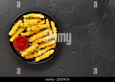 Fried zucchini sticks on plate over dark stone background with copy space.  Top view, flat lay Stock Photo