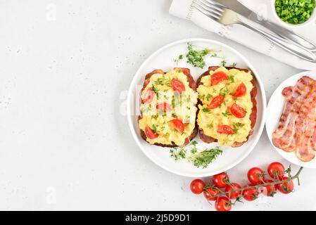 Scrambled eggs with microgreen, bacon and tomatoes on bread over light stone background with copy space. Top view, flat lay Stock Photo