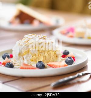 meringue roll with strawberries, blueberries, raspberries and cranberries. Dessert decorated with fresh berries on table. Stock Photo