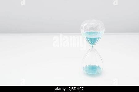 Hourglass on bright light, sandglass with blue sand on white background Stock Photo