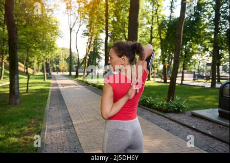 Muscular fit athlete, middle aged confident sportswoman raising arms up, stretching out and warming up her body before morning jog along the city park Stock Photo
