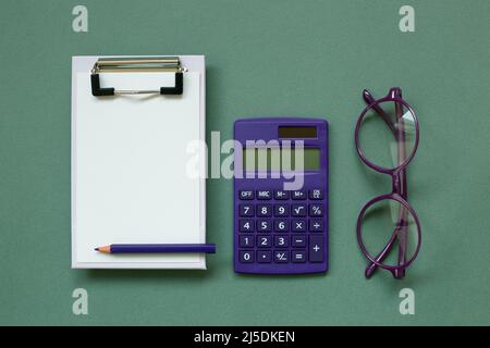 Clipboard and paper sheet, calculator, glasses on green background. top view, copy space Stock Photo