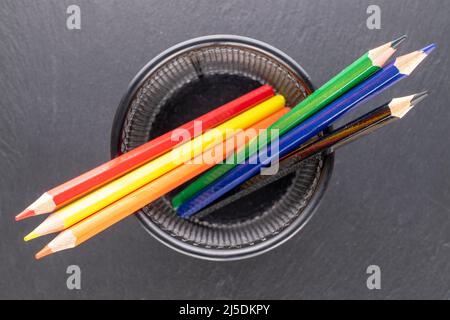 Several colored pencils in a metal glass on a slate stone, macro, top view. Stock Photo