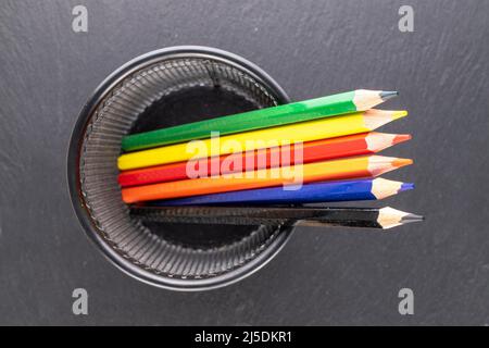 Several colored pencils in a metal glass on a slate stone, macro, top view. Stock Photo