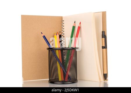 Several colored pencils in a metal glass with a notebook, close-up, isolated on a white background. Stock Photo