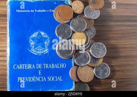 Translation: Federative Republic of Brazil, Ministry of Labor. Work Card (Carteira de trabalho) next to Brazilian real coins, Brazilian money. Stock Photo