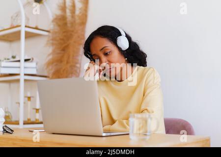 Bored and tired African-American female student watching online distance class on laptop Stock Photo