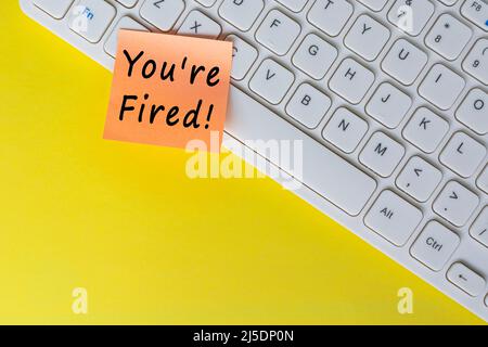 You're Fired text on orange sticky note on top of white keyboard. Human Resource and contract concept. Stock Photo