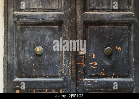 Close-up of a weathered black wooden door with metal handles and scratched wood, Italy Stock Photo