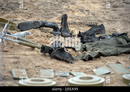 KYIV REGION, UKRAINE - APRIL 21, 2022 - Boots and the pieces of Russian uniforms as well as explosives are arranged on the ground during a mine cleara Stock Photo