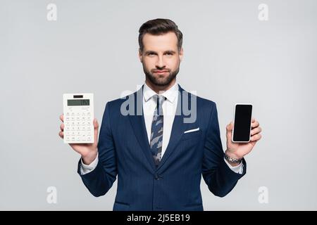 economist in blue suit showing calculator and smartphone with blank screen isolated on grey Stock Photo
