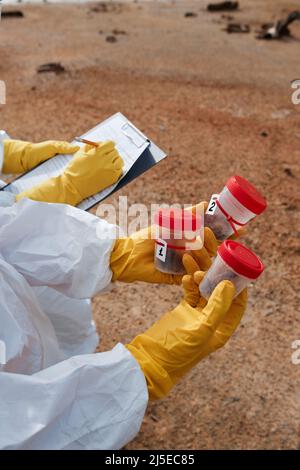Close-up of unrecognizable environmental scientist making notes in clipboard while colleague holding containers of polluted soil samples Stock Photo