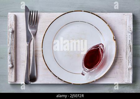 Empty aged white ceramic plate with berry sauce in a gravy boat and cutlery