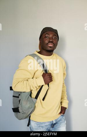 Portrait of serious handsome Black student guy in yellow sweatshirt and cap standing with satchel against isolated baclground Stock Photo