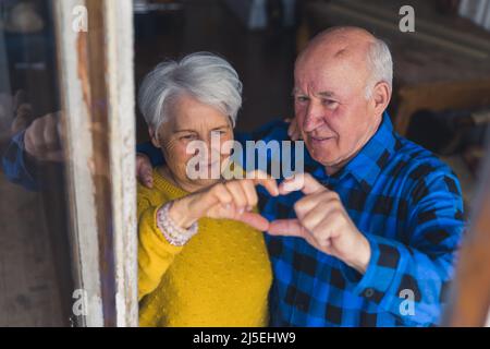 long and happily - cute senior couple making hear shape with fingers medium closeup from above living room senior people support concept. High quality photo Stock Photo