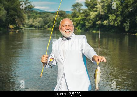 Portrait of cheerful senior man fishing. Grandfather with catch fish. Mature  man fisherman in white suit and bowtie with fishing rod, spinning reel on  Stock Photo - Alamy