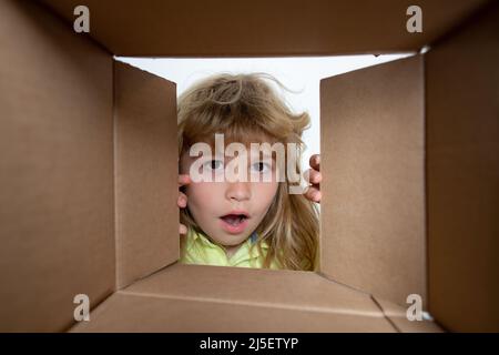 Kid boy unpacking and opening carton box looking inside with surprise face. Kid opening package. Stock Photo