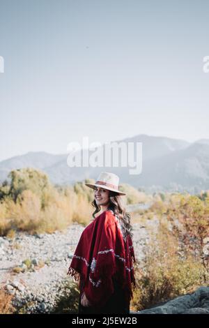Traditional latin american woman wearing a red poncho and a hat, in a natural space. Womens empowerment Stock Photo