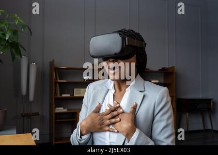 Emotional shocked african businesswoman in VR headset immersed in 3D virtual world screaming wow Stock Photo