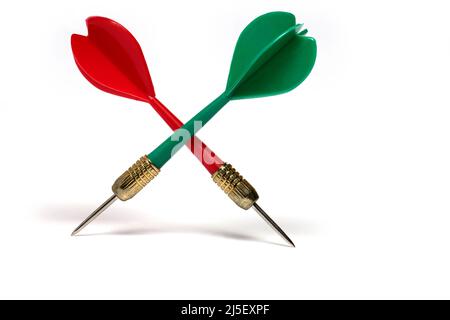 Close up of one red and green dart with pointed metal tip crossed in shaft area on white background and visible shadows Stock Photo