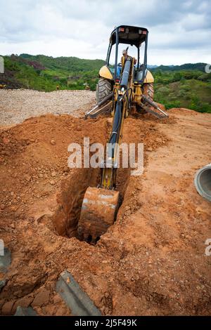 An excavator operator with an excavator machine is digging a ditch on a construction site in Las Minas de Tulu, Cocle province, Republic of Panama. Stock Photo