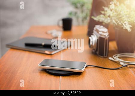 Charging the smartphone with wireless charger on desktop. Stock Photo