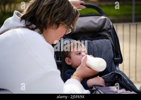 Mother giving a bottle of milk to her son while enjoying the day in the park. Stock Photo