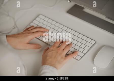Close-up photo of woman’s hands typing on a wireless white aluminum keyboard. Stock Photo